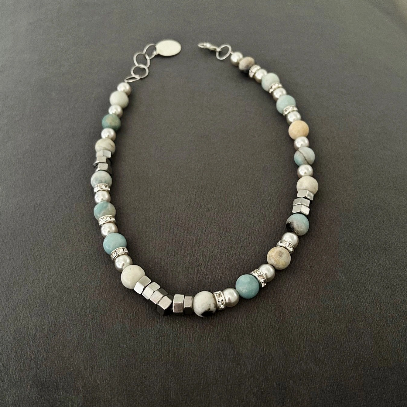 Ett snyggt armband med amazonit stenar i toner av vitt, grått, beige och turkos. Smycket pryds även av fina detaljer med inslag av strass-stenar.