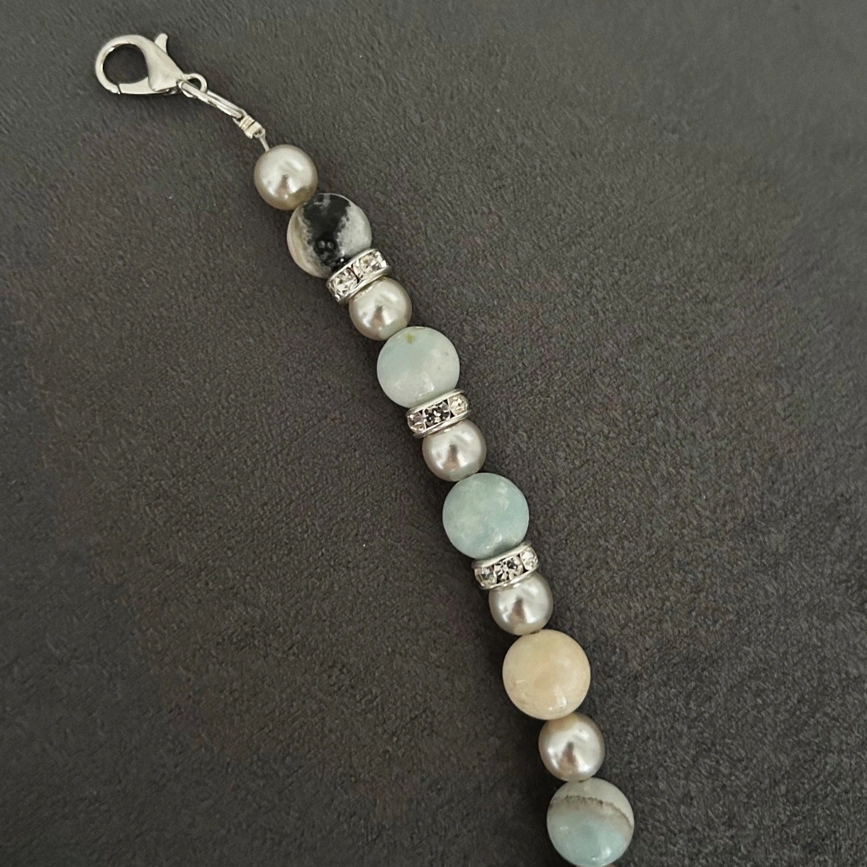 Ett snyggt armband med amazonit stenar i toner av vitt, grått, beige och turkos. Smycket pryds även av fina detaljer med inslag av strass-stenar.