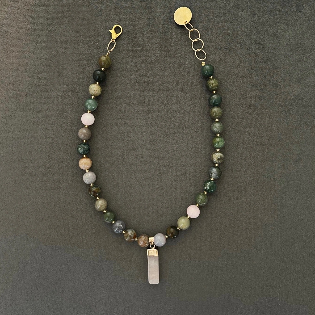 Halsband med halvädelstenar (agatsten), detta förgylls med indiska naturstens-agater. Smycket går i jordnära toner med skiftningar i lila och grå, med inslag av jadesten i rosa ton. Halsbandet pryds också med ett hänge i vacker rosenkvarts.