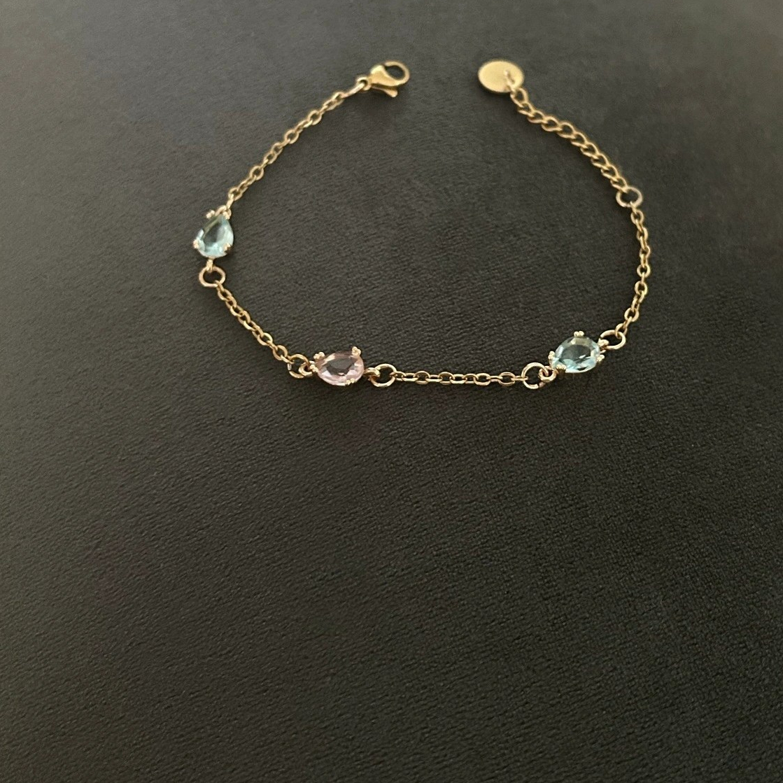 Ett fint armband i smal guldkedja som förses med dekorativa glasstenar i rosa och havsblå nyans.