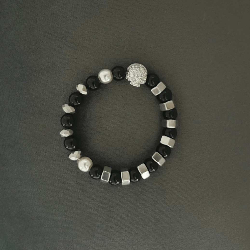 Snyggt armband i den rockiga stilen med svarta toner. Vaxade svarta, facetterade glaspärlor och silver-muttrar. Hänge med döskalle i strass tillför smycket en snygg detalj!