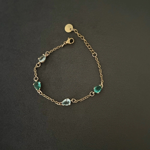 Ett fint armband i smal guldkedja som förses med dekorativa glasstenar i smaragdgrön och turkos/havsblå nyans.