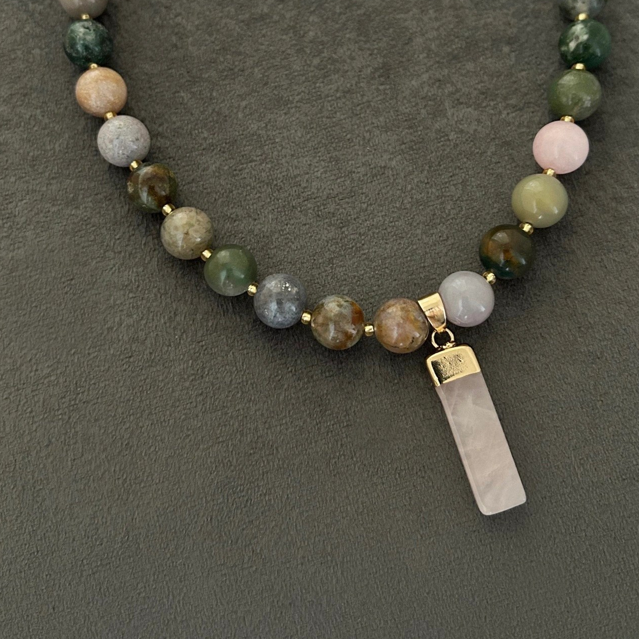 Halsband med halvädelstenar (agatsten), detta förgylls med indiska naturstens-agater. Smycket går i jordnära toner med skiftningar i lila och grå och med inslag av jadesten i rosa ton. Halsbandet pryds också med ett hänge i vacker rosenkvarts.