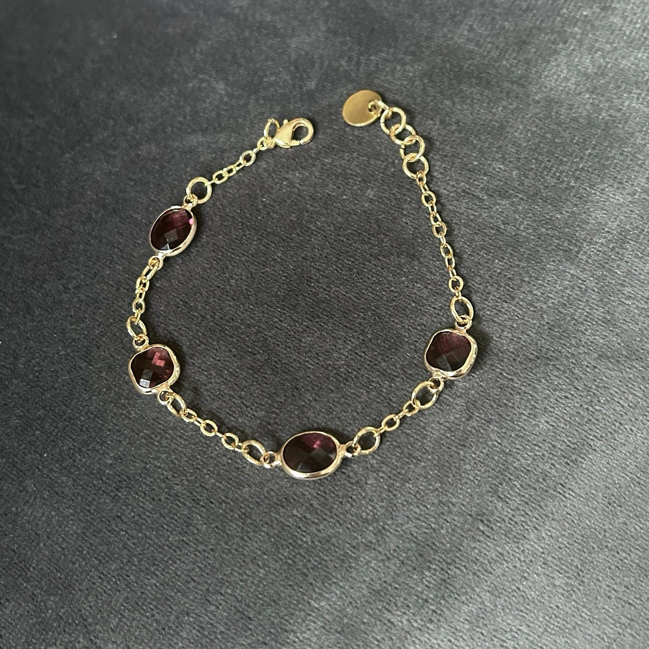 Ett smakfullt armband med smal kedja i guldfärgad nyans med fyra tindrande glasstenar i fina lila skiftningar.