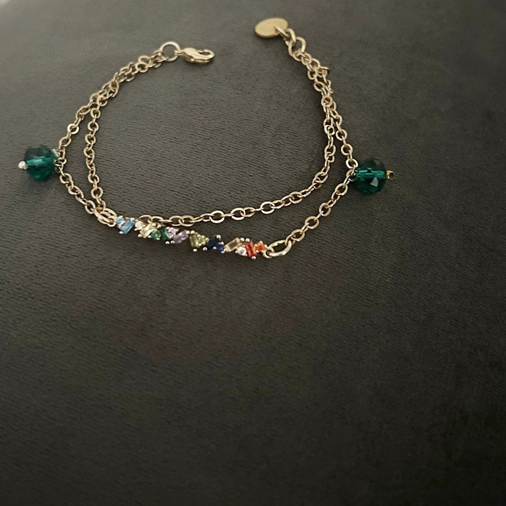 Ett enkelt och prydligt Armband av kedja i guldnyans. Dekorativa stenar med färger i röd, blå, grön, lila och facetterade smaragdgröna glaspärlor förgyller detta smycke.