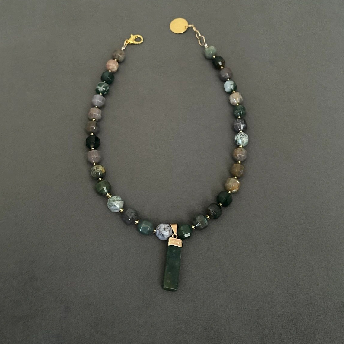 Halsband med halvädelstenar (agatsten), detta förgylls med indiska agater i en dekorativ kantig form på stenen. Smycket går i jordnära toner med vissa skiftningar i lila och grå. Halsbandet pryds också av ett hänge i moss-agat.