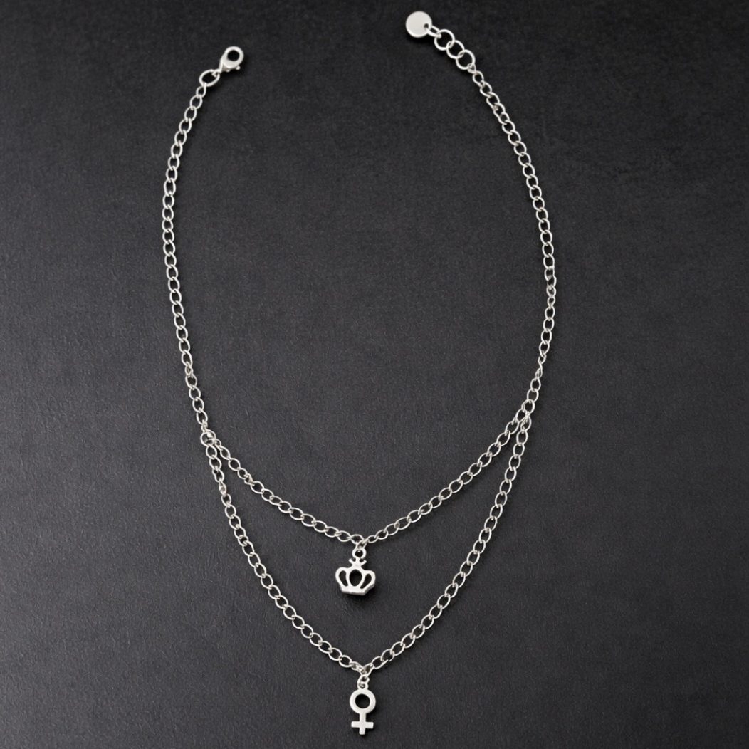 Halsband i silvernyans med dubbelkedja nedtill. Smycket förses med två dekorativa berlocker i form av kvinnosymbol och en krona.
